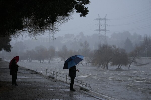 A couple walks on the edge of the Los Angeles River on Feb. 4, 2024, as an atmospheric rivers batters Los Angeles. (AP Photo/Damian Dovarganes, File)